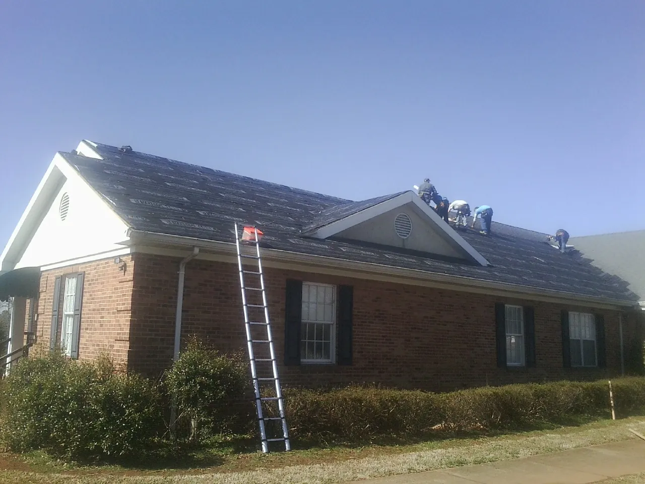 Crew tearing shingles off a brick ranch roof with a ladder set — Metal Roof Repair work by our crew in Catonsville