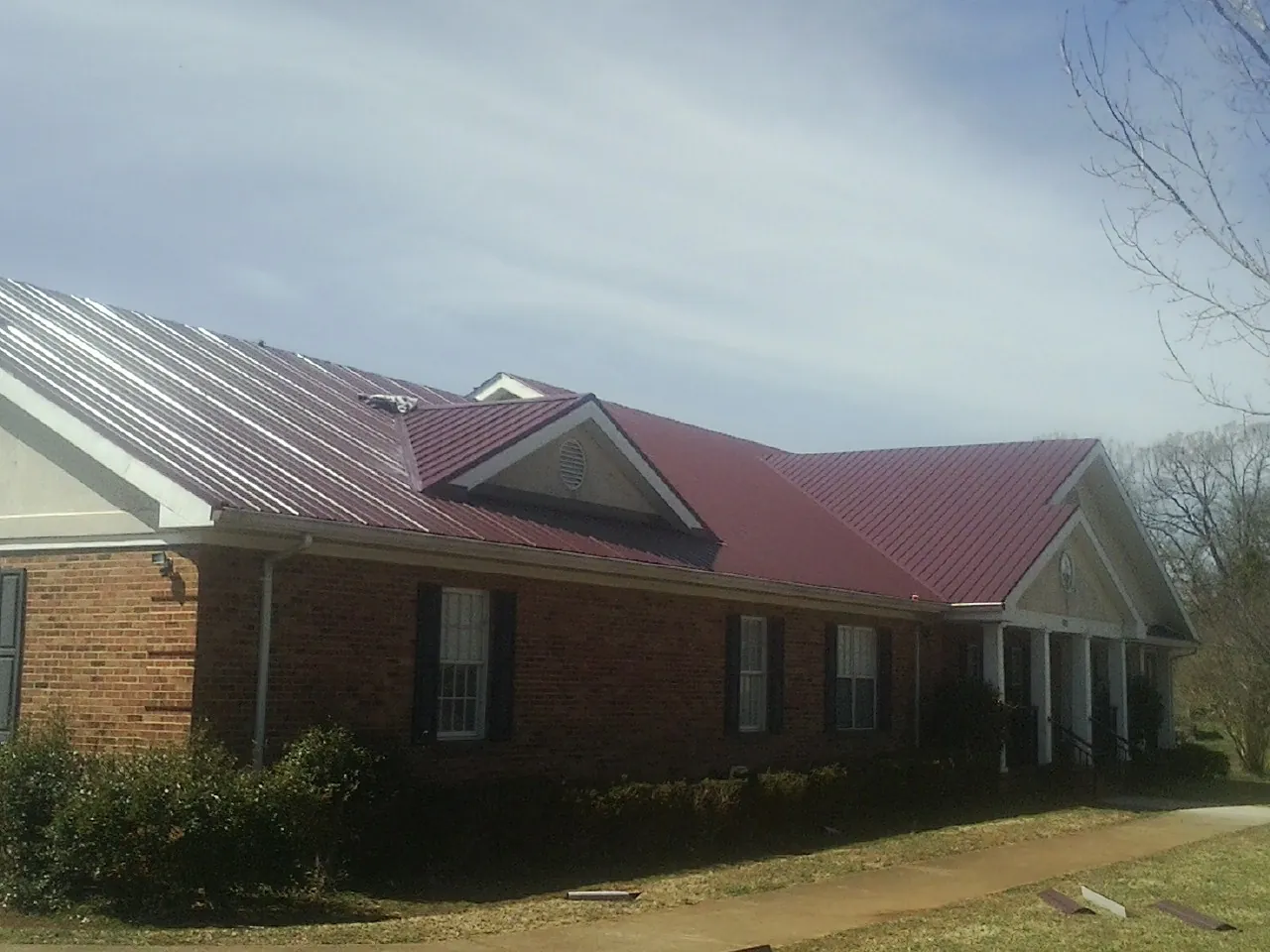 Red metal roof with gabled entries on a long brick building, from a Hail Damage Roof Repair job in Catonsville