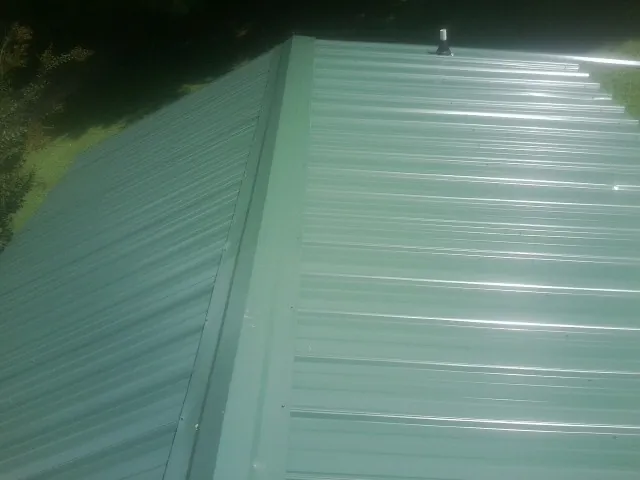 New green metal panels meeting at the ridge of a roof — Flat Roof Repair work by our crew in Catonsville