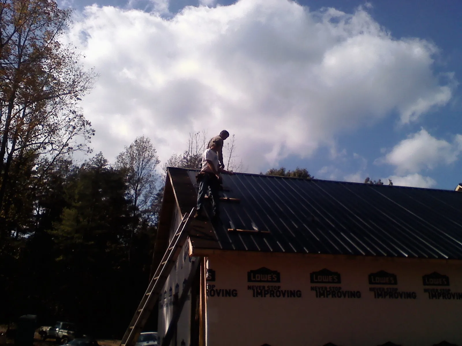 Roofer fastening dark metal panels high against a cloudy sky, from a Roof Inspection job in Catonsville