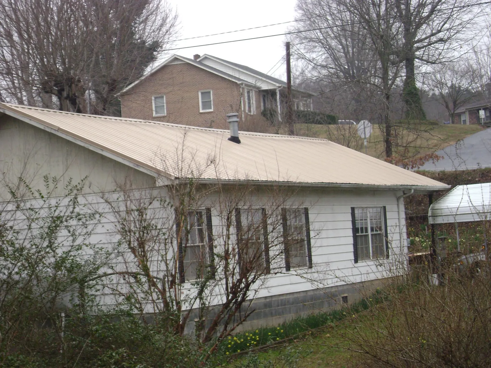 Tan metal roof on a white sided house set into a hillside — Commercial Roofing by Roofing Brothers in Catonsville
